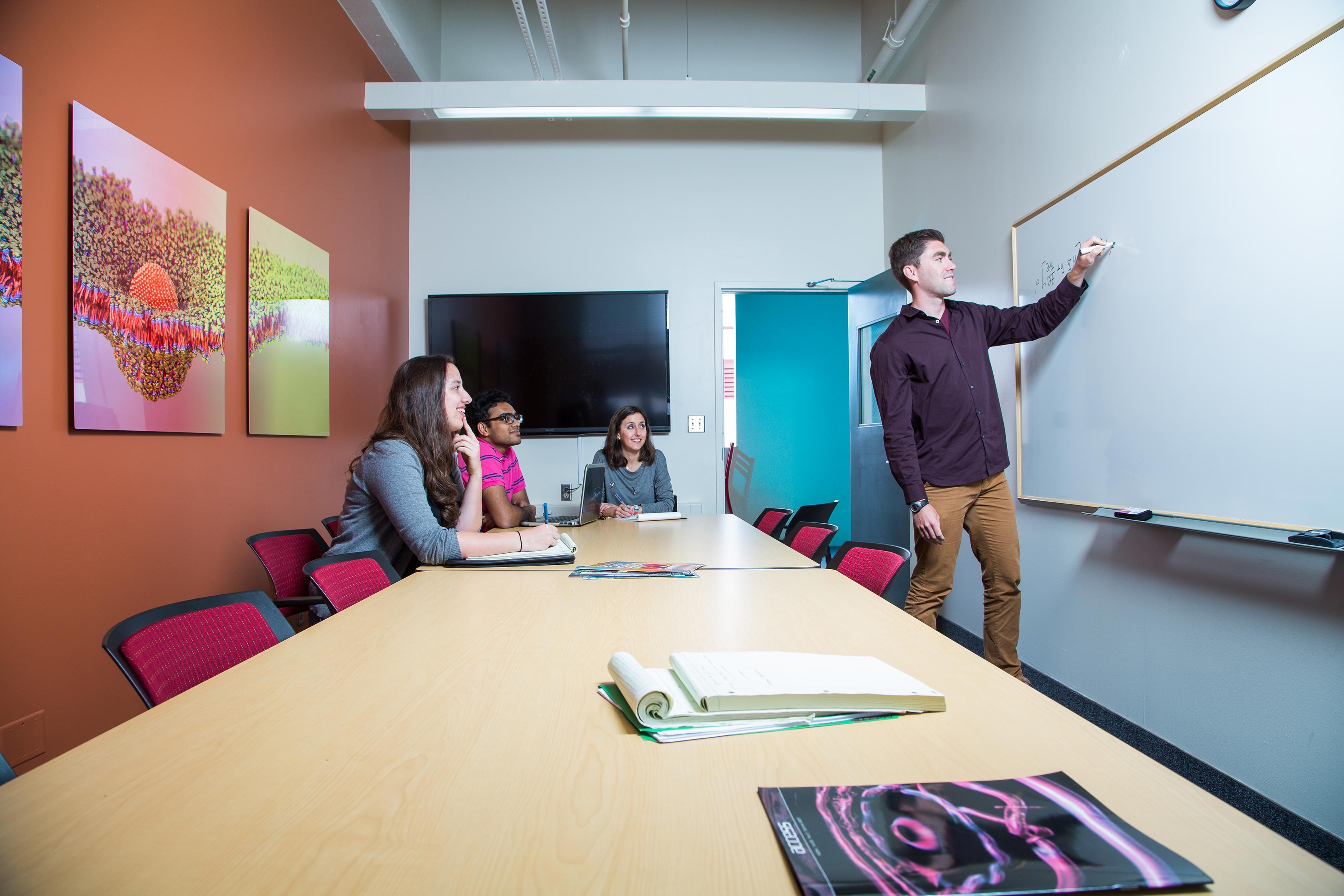 Students at table and one standing and drawing on whiteboard