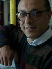 headshot of Khaled, smiling and wearing black rimmed glasses