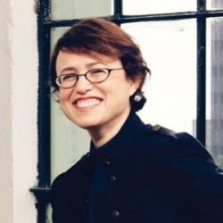 headshot of Leana, wearing a black turtle neck and black rimmed glasses, smiling