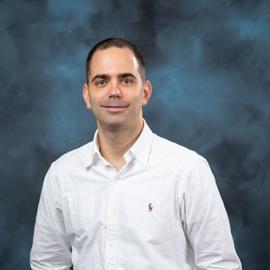 headshot of Theodore from the waist up, wearing a light blue collared shirt, smiling