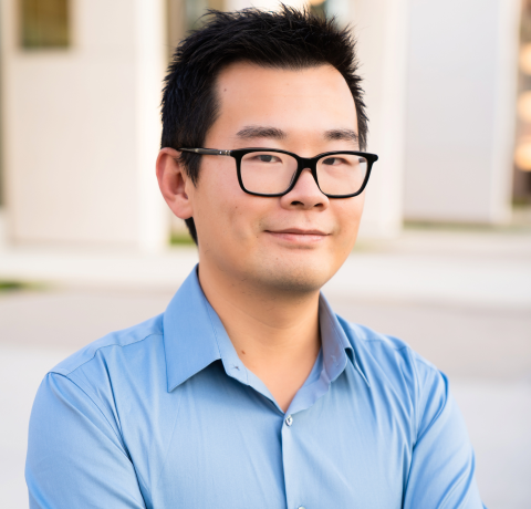 headshot of William Wang from the shoulders up in a light blue collared shirt and black rimmed glasses, smiling