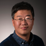 headshot of Xifeng wearing a blue plaid shirt and black jacket, smiling