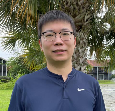 headshot of Yuheng, wearing a navy sweater and black rimmed glasses, smiling