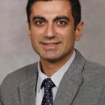 headshot of Amir, wearing a grey suit, smiling