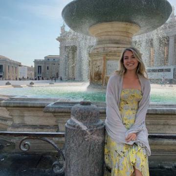 photo of Ashley, sitting in front of a fountain, wearing a yellow dress, smiling