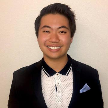 headshot of Justin, wearing a polka dotted collared shirt and black blazer, smiling