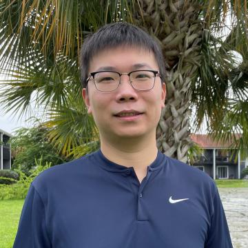 headshot of Yuheng, wearing a navy sweater and black rimmed glasses, smiling