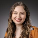 headshot of Bella Cardoso, from the shoulders up, wearing an orange floral blouse and red-orange lipstick